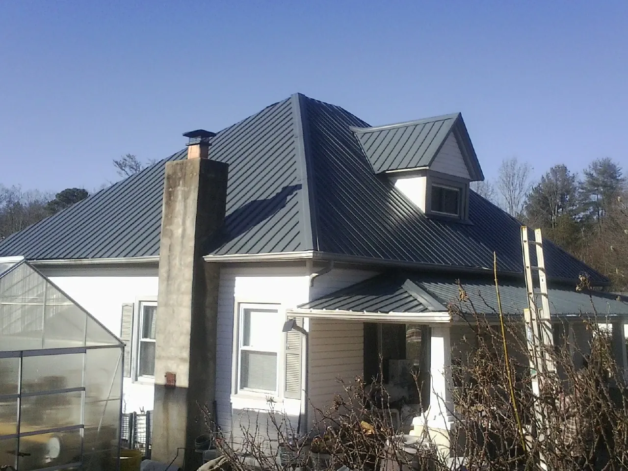 Dark blue standing seam metal roof on a white farmhouse with dormer — Slate & Tile Roof Repair by Roofing Brothers in Mayville