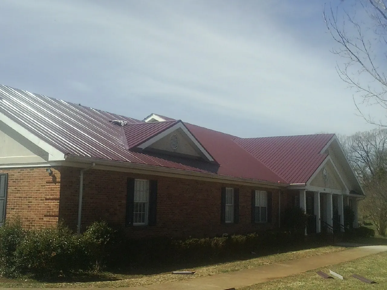 Red metal roof with gabled entries on a long brick building, from a Hail Damage Roof Repair job in Mayville