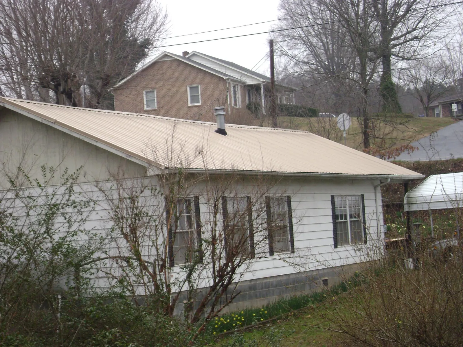 Tan metal roof on a white sided house set into a hillside — Commercial Roofing by Roofing Brothers in Mayville